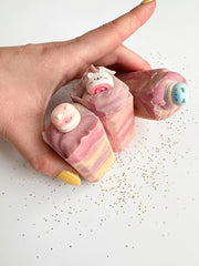 A hand holding two bedtime honey soap bars showing the swirl and the charm toppers