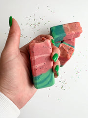 A hand holding a watermelon soap bar showing its coral and green layers