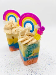 Two rainbow striped soap bars with piped tops and rainbow toppers on a white background