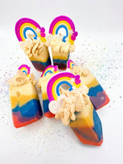 Rainbow striped handmade soap bars scattered on a white surface with piped cream tops